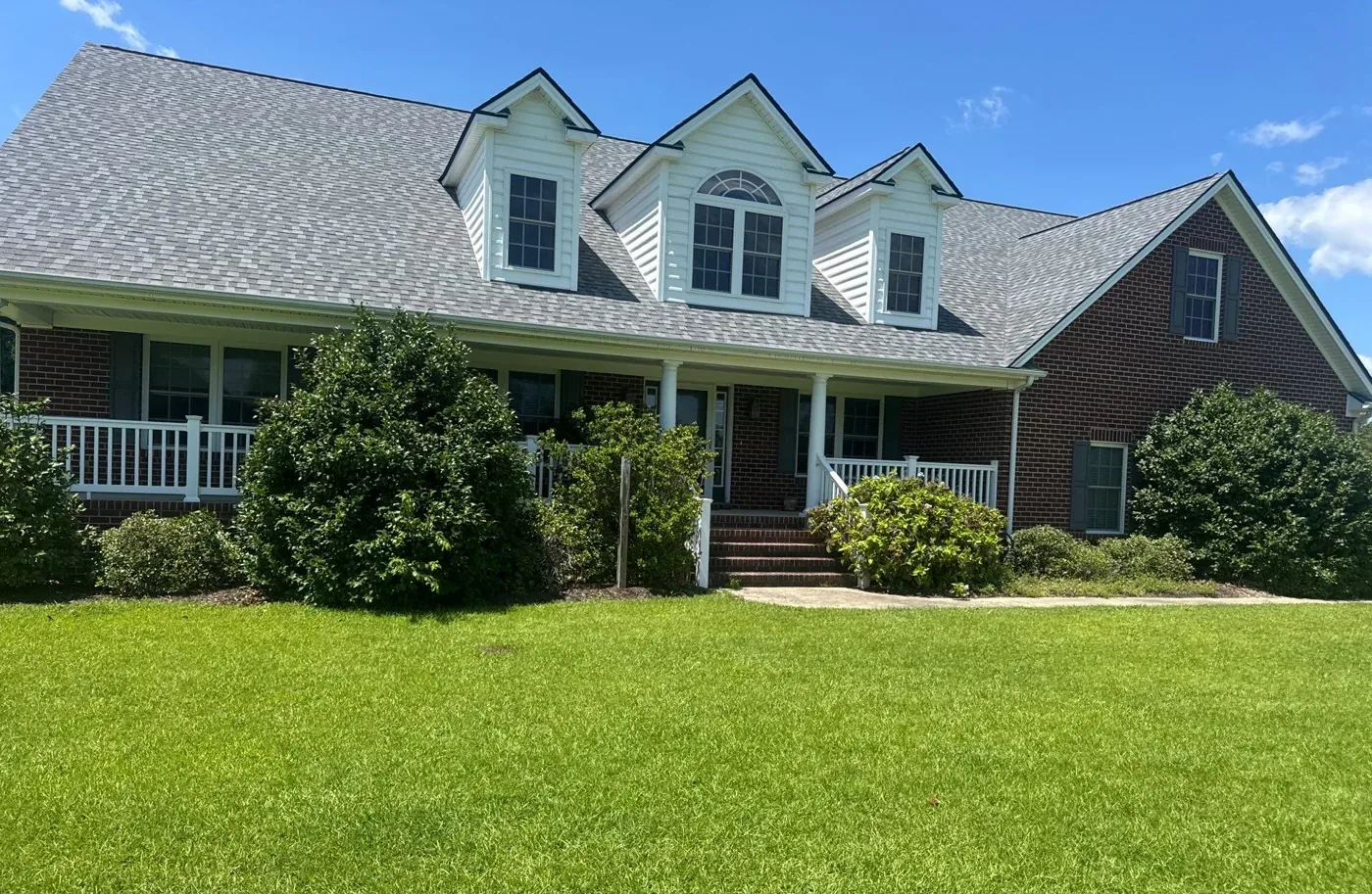 Completed roof on a brick home in Eastern North Carolina, photographed from the front lawn under a clear sky.