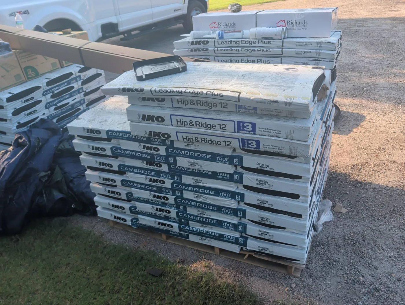 Pallet of IKO Cambridge architectural shingles in charcoal grey with IKO Hip and Ridge 12 caps and starter staged on a driveway