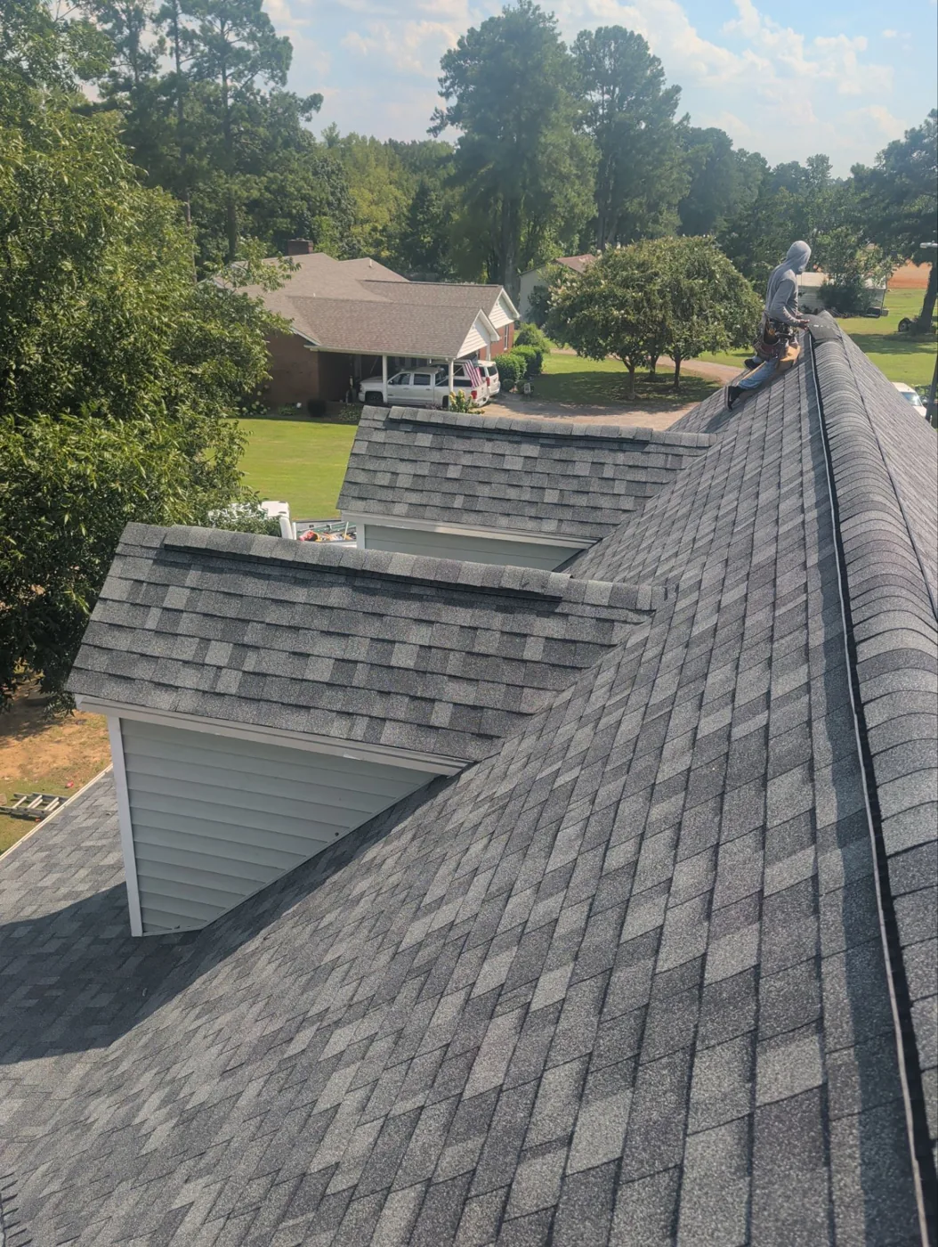 Completed roof photographed from the ridge, showing new charcoal architectural shingles across the main slopes, two finished dormers and a clean capped ridge running to the far end.