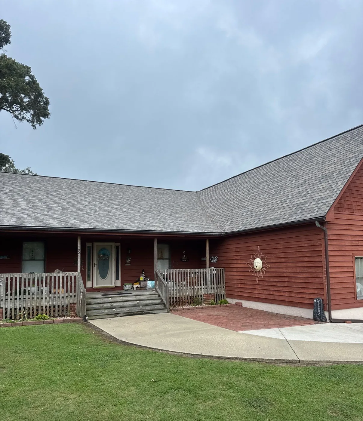 The completed home seen from the front lawn, the red-stained wood-sided house with its covered porch now under a new grey architectural shingle roof.