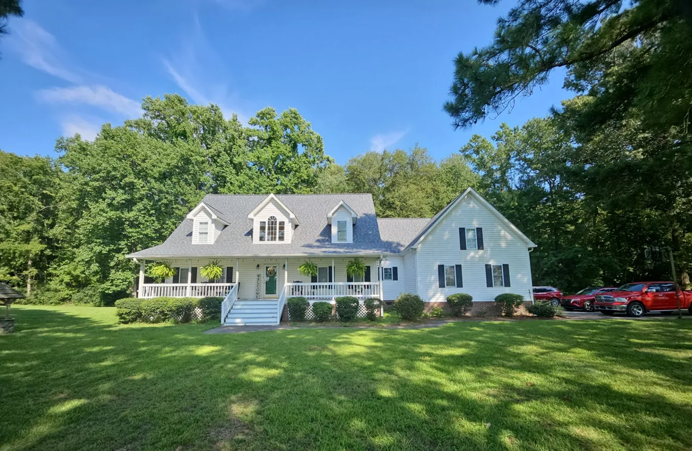 The completed home photographed from the front lawn, the white-sided house with black shutters and covered porch now under a new grey architectural shingle roof under a clear blue sky.