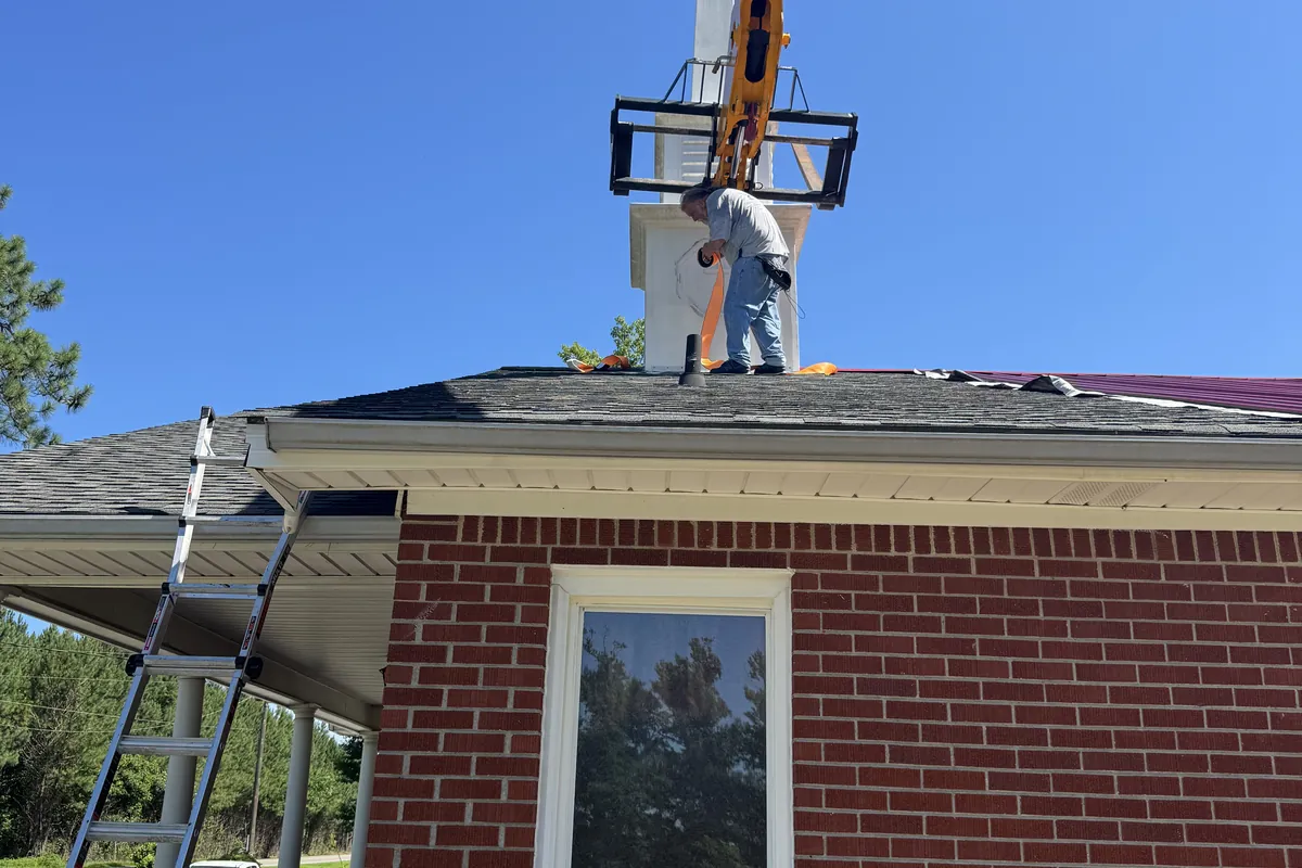 Crane lifting a church steeple into place on a brick sanctuary