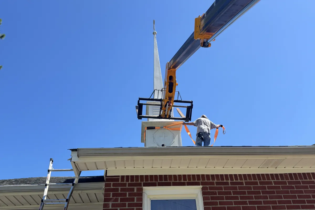 Steeple being set onto a brick church roof by crane